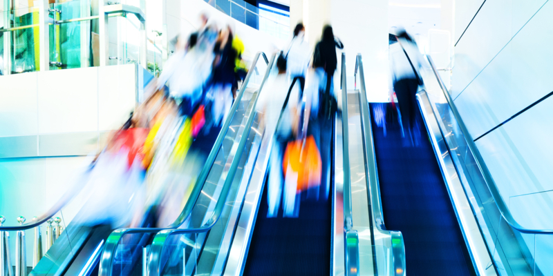 people rushing in escalators at a modern shopping mall.