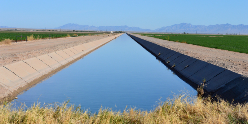 Large irrigation canal filled with water between two agricultural fields near Blythe, California.