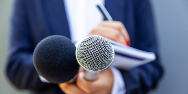 News reporter or TV journalist at press conference, holding microphone and writing notes