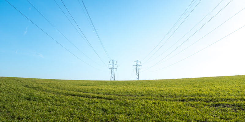 Large pylons with power lines stretching across a green grass field against a blue sky