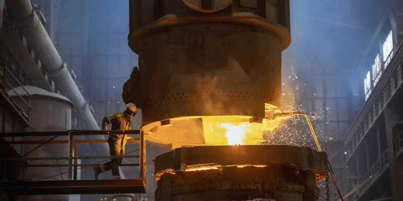 Steelworker inspecting molten steel during steel pour in steelworks